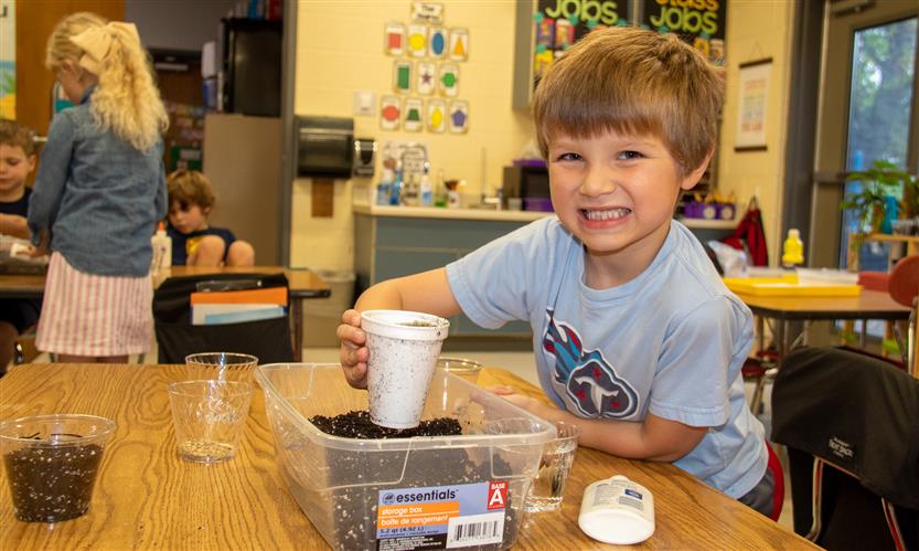 A blond boy smiles while getting a cup full of dirt.